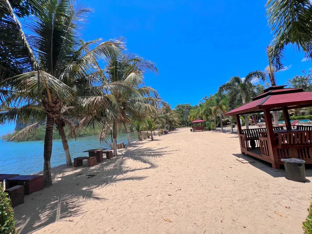 A red-roofed sala on the sand between coconut palms
