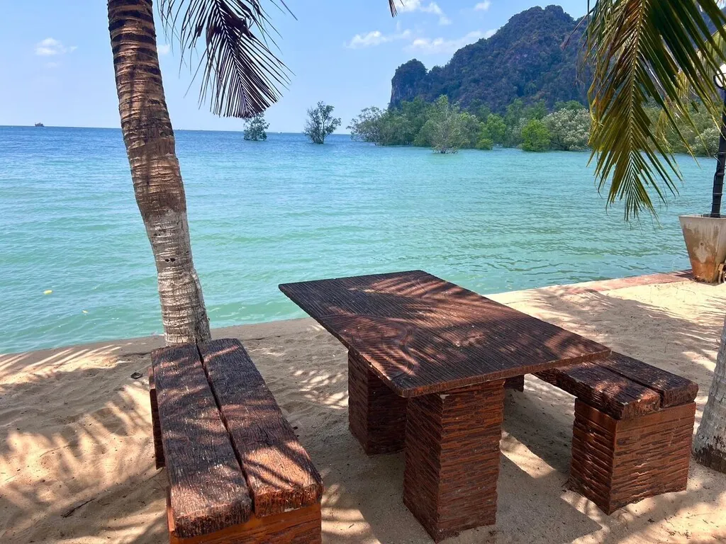A teak picnic table on the sand facing limestone islands