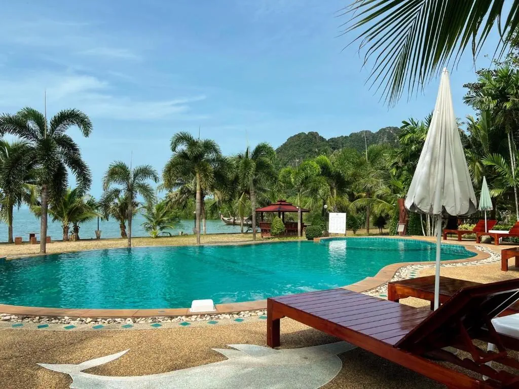 A teak sun lounger by the pool, with the sea and cliffs beyond