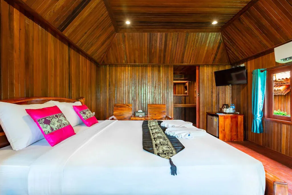 A teak cottage interior with a king bed and bright cushions
