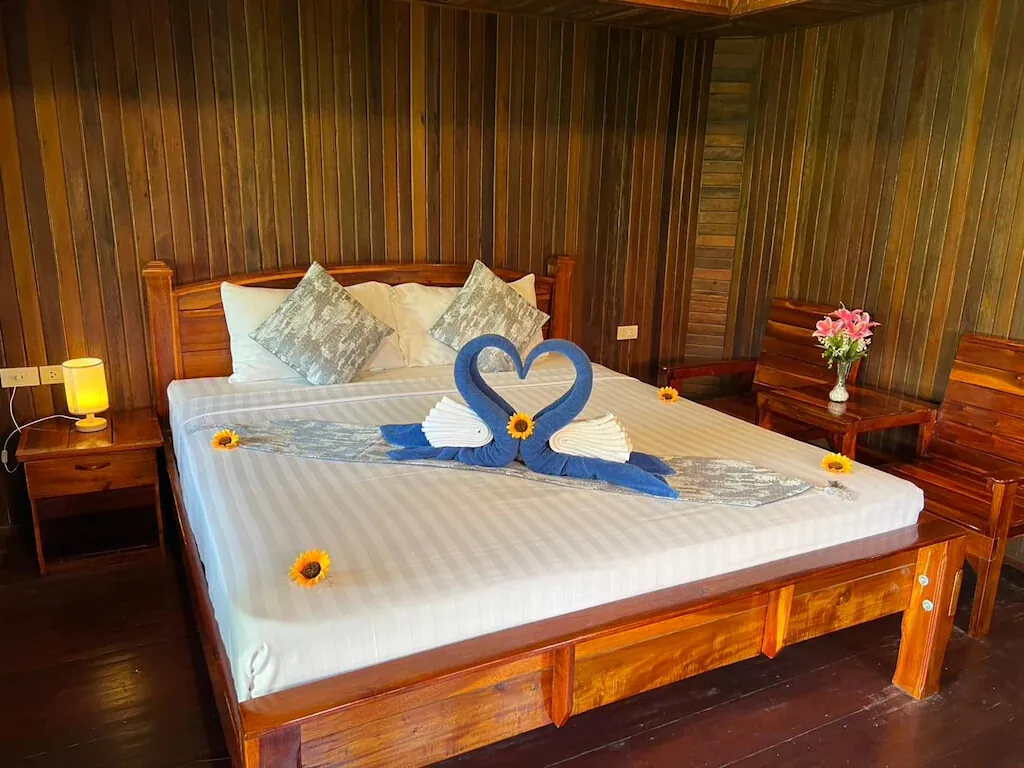 A double bed dressed with towel swans in a warm teak room